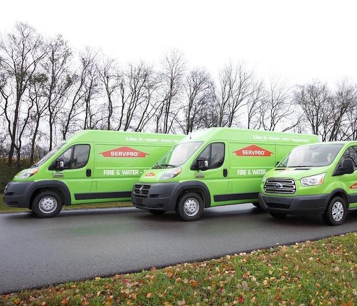 "three green SERVPRO trucks lined up on a side street
